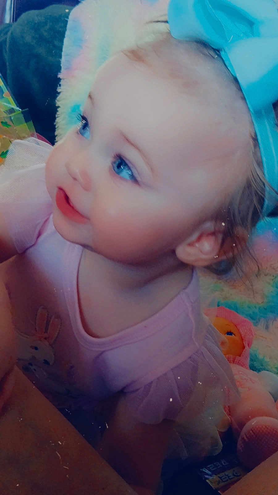Addisynn is registered to the contest to win money with this photo: toddler, child, blue_eyes, pink_clothing, bow, headband, soft_toys, doll, indoor, cute, baby, portrait, curious, blonde_hair, face, smiling, closeup, infant, playful, colorful_background