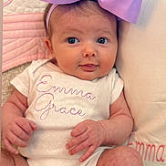 Emma Grace is registered to the contest to win money with this photo: baby, infant, bow, headband, onesie, clothing, face, hands, legs, pillow, quilt, text_embroidery, cute, portrait, child, soft_texture, pink, purple, newborn, smiling