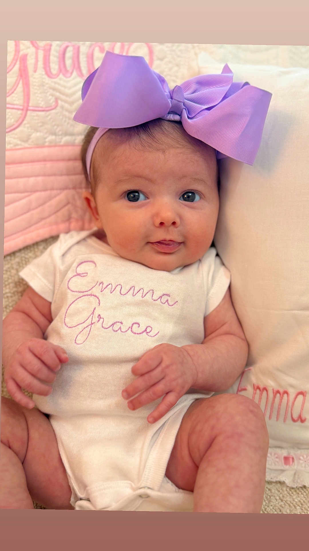 Emma Grace is registered to the contest to win money with this photo: baby, infant, bow, headband, onesie, clothing, face, hands, legs, pillow, quilt, text_embroidery, cute, portrait, child, soft_texture, pink, purple, newborn, smiling