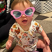 Raelynn joined the competition — help win amazing prizes! toddler, child, sunglasses, pink, heart_shaped, onesie, floral, messy, indoor, carpet, laundry_basket, toy, playful, cute, face, person, baby, floor, lighting, expression