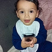 Issac participe au concours pour gagner de l'argent avec cette photo : toddler, child, baby, bib, couch, blanket, pillow, clothing, indoor, person, face, hair, eyes, hands, sitting, toy, remote, expression, cute, cozy