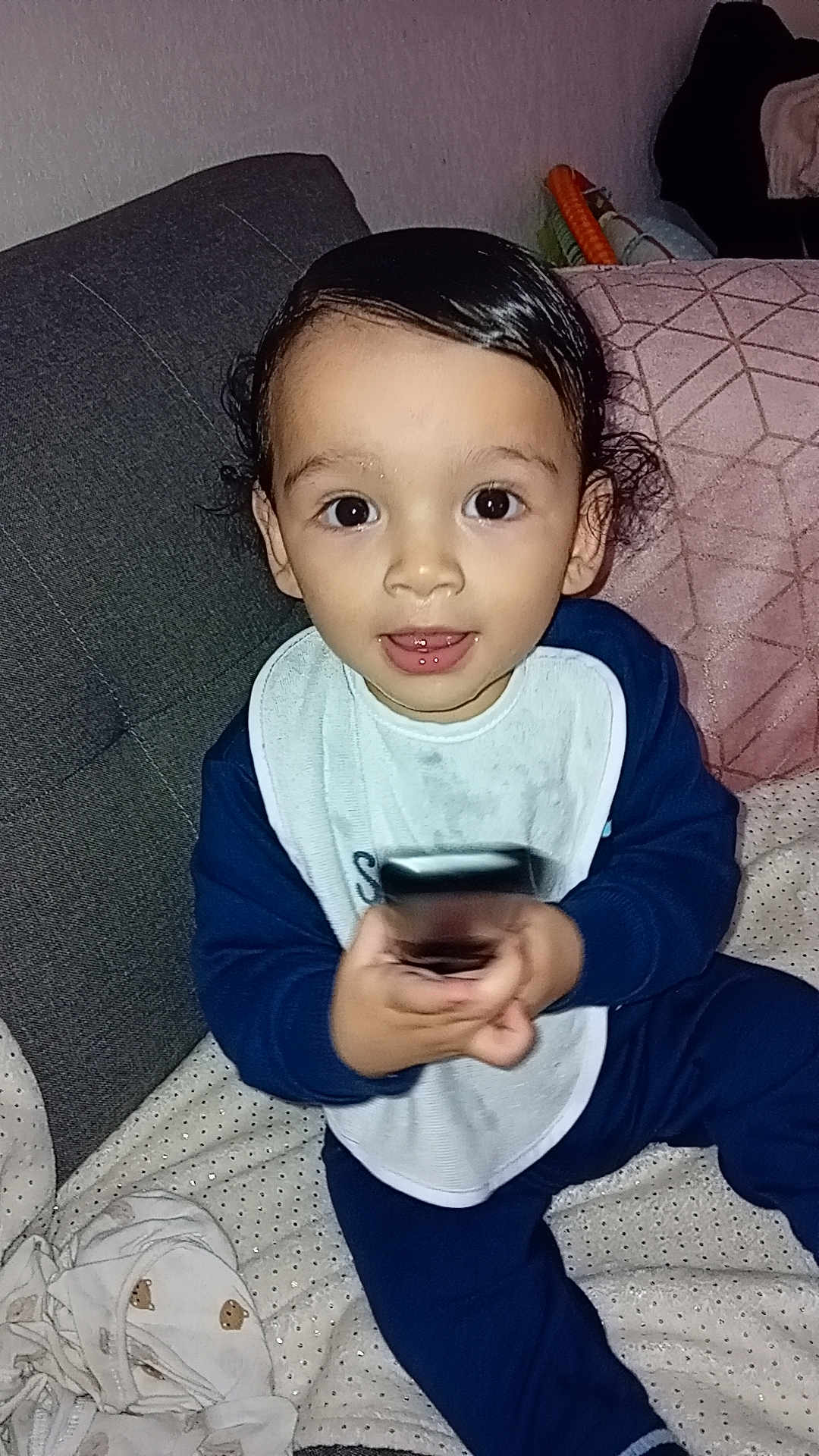 Issac participe au concours pour gagner de l'argent avec cette photo : toddler, child, baby, bib, couch, blanket, pillow, clothing, indoor, person, face, hair, eyes, hands, sitting, toy, remote, expression, cute, cozy