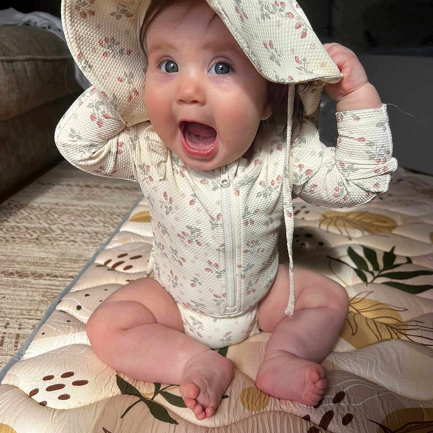 Scottie Lou joined the competition — help win amazing prizes! baby, child, clothing, couch, cute, expression, floral_pattern, happy, hat, indoor, infant, mat, person, playful, portrait, sitting, skin, smiling, young_child, zipper