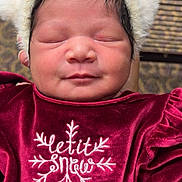 Elizah is registered to the contest to win money with this photo: baby, newborn, infant, sleeping, face, hat, pom_pom, velvet_dress, burgundy, embroidery, snowflake, closeup, portrait, cozy, chubby_cheeks, dark_hair, seated, indoor, patterned_carpet, subtle_smile