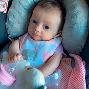 Emma is registered to the contest to win money with this photo: baby, infant, bib, bottle, plush_toy, blanket, seat, cushion, clothing, cute, child, indoors, soft, comfort, portrait, feeding, pink, striped_blanket, newborn, resting