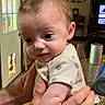 Emma is registered to the contest to win money with this photo: baby, infant, hands, polka_dot, clothing, kitchen, countertop, curious, expression, indoor, person, cute, face, adult, holding, window, curtains, furniture, television, home