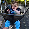 baby, child, swing, playground, outdoor, park, smiling, thumb_sucking, blue_pants, black_swing, sunlight, shadow, fence, stroller, person, casual_clothing, curly_hair, barefoot, happy, daytime