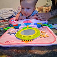 Isabel joined the competition — help win amazing prizes! baby, blanket, child, colorful, cute, early_learning, engagement, expression, face, floor, hands, indoor, infant, mirror_toy, nail_polish, person, play_mat, soft_toy, tattoo, toy