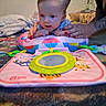 baby, blanket, child, colorful, cute, early_learning, engagement, expression, face, floor, hands, indoor, infant, mirror_toy, nail_polish, person, play_mat, soft_toy, tattoo, toy