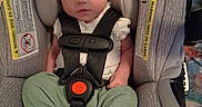 Isabel is registered to the contest to win money with this photo: baby, car_seat, child, clothing, cute, face, green_pants, head_support, indoor, infant, looking, person, portrait, safety, seatbelt, sitting, straps, warning_label, white_socks, young_child