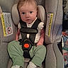 baby, car_seat, child, clothing, cute, face, green_pants, head_support, indoor, infant, looking, person, portrait, safety, seatbelt, sitting, straps, warning_label, white_socks, young_child