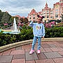 castle, child, cloudy_sky, flowers, fountain, frozen_character, girl, greenery, jeans, minnie_mouse_ears, outdoor, pavement, peace_sign, pink_building, smile, sneakers, sweatshirt, theme_park, tourist, vacation
