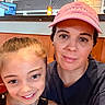 child, woman, smile, face, portrait, indoor, hat, cap, brown_eyes, blonde_hair, short_hair, casual_clothing, restaurant, light, wooden_ceiling, television, wall, person, happy, together