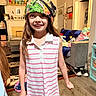 Alyssa is registered to the contest to win money with this photo: child, girl, smiling, bandana, striped_dress, indoor, living_room, furniture, sofa, rug, ceiling_fan, toy_figures, wood_floor, casual_clothing, home_decor, portrait, happy, person, long_hair, colorful