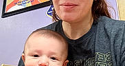 Jeremy joined the competition — help win amazing prizes! baby, brown_hair, cap, casual_clothing, child, closeup, cute, face, framed_sign, graphic_tee, happy, holding, indoor, orange_shirt, person, portrait, purple_wall, seated, smile, woman