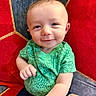 Jeremy is registered to the contest to win money with this photo: baby, blue, casual_clothing, child, closeup, colorful_background, cute, dinosaur_print, gesture, green_shirt, happy, indoors, infant, patterned, person, portrait, red, short_hair, sitting, smiling
