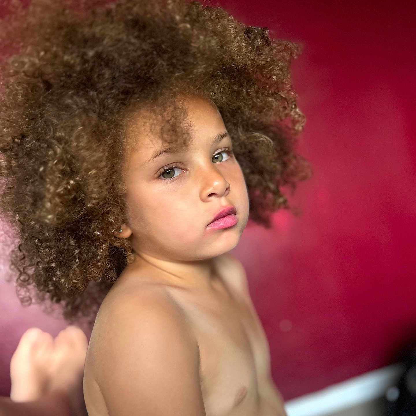 Jasmine Keira participe au concours pour gagner de l'argent avec cette photo : bare_chest, child, closeup, contemplative, curly_hair, expression, eyebrows, eyes, face, head, indoor, lips, natural_light, person, portrait, red_background, serene, shoulder, skin, young