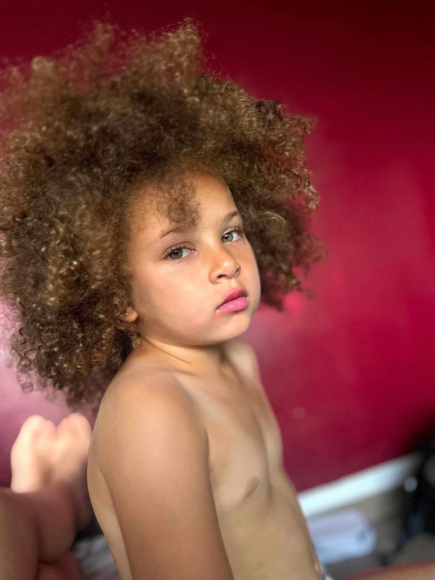 Jasmine Keira participe au concours pour gagner de l'argent avec cette photo : bare_chest, child, closeup, contemplative, curly_hair, expression, eyebrows, eyes, face, head, indoor, lips, natural_light, person, portrait, red_background, serene, shoulder, skin, young