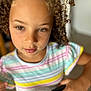 child, curly_hair, hazel_eyes, striped_shirt, indoor, handlebar, close_up, portrait, person, young, casual_clothing, focus, blurry_background, hand, skin, expression, cute, curly, toddler, colorful