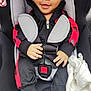 baby, car_seat, child, infant, smiling, black_clothing, red_clothing, socks, blanket, safety_harness, seat_belt, cute, happy, portrait, indoor, close_up, person, young_child, baby_clothes, comfort
