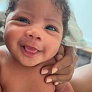 Ahmaad joined the competition — help win amazing prizes! baby, infant, child, portrait, smiling, happy, tongue_out, curly_hair, close_up, face, eyes, skin, diaper, adult_hand, caregiver, indoor, window, natural_light, sitting, candid