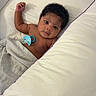 baby, infant, child, portrait, lying_down, bed, bedding, blanket, pillow, pacifier, curly_hair, dark_hair, brown_skin, wide_eyes, awake, indoor, bedroom, cozy, candid, photography