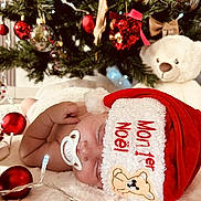 Hannah a rejoint le concours — aidez-le/la à gagner de superbes lots ! baby, sleeping, pacifier, santa_hat, christmas_tree, ornaments, red_balls, teddy_bear, blanket, fairy_lights, holiday, festive, cute, infant, soft_texture, decorations, indoors, celebration, cozy, christmas
