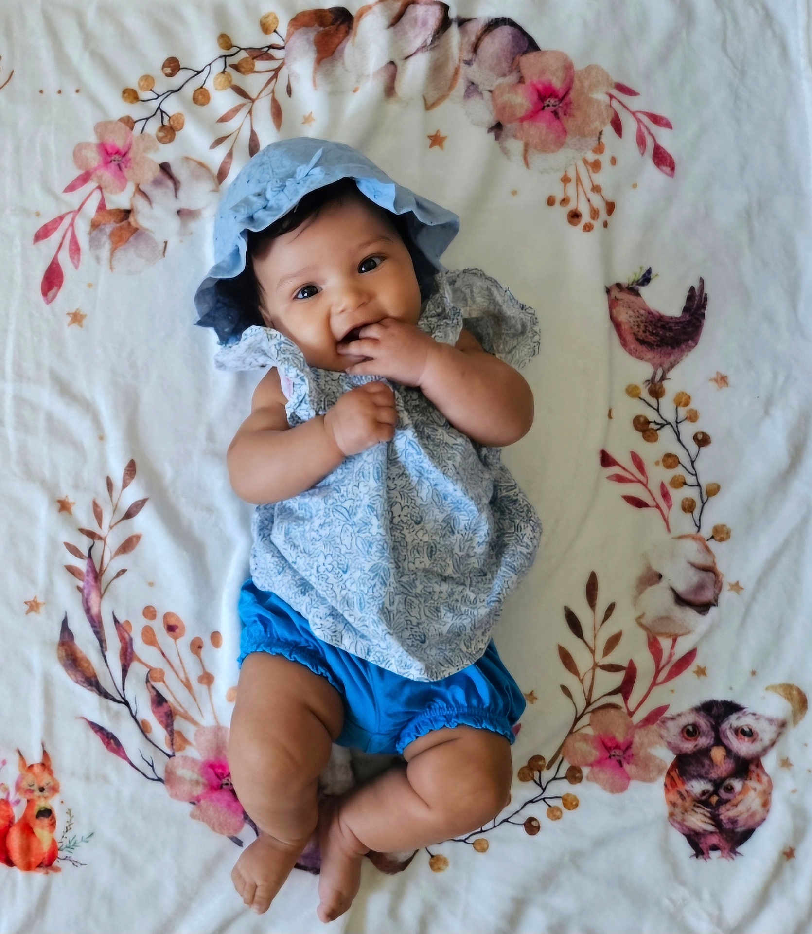Mia a rejoint le concours — aidez-le/la à gagner de superbes lots ! baby, infant, child, blue_bonnet, blue_shorts, blanket, floral_pattern, animal_pattern, hands, legs, smiling, chewing_fingers, cute, lying_down, indoors, soft_texture, happy, portrait, adorable, bright_eyes