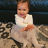 Mia a rejoint le concours — aidez-le/la à gagner de superbes lots ! toddler, child, smiling, clapping, sitting, pink_bows, white_shirt, tulle_skirt, patterned_rug, leather_couch, happy, indoor, cute, young_child, playful, baby, small_hands, floor, portrait, fun