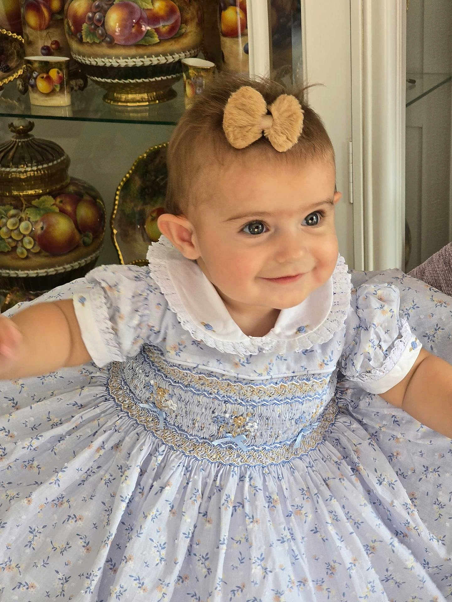 Diana joined the competition — help win amazing prizes! toddler, child, smile, dress, bow, blue, floral_pattern, face, eyes, indoor, cabinet, ceramics, fruit_pattern, furniture, portrait, cute, happy, person, young_child, clothing