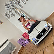 Inaya participe au concours pour gagner de l'argent avec cette photo : balloons, birthday, celebration, child, dress, floor, gifts, girl, hair_ties, headlights, indoor, party, person, photography, pink, presents, tile_floor, toy_car, wall, white