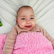Aria is registered to the contest to win money with this photo: baby, smiling, blanket, pink, infant, cute, face, child, happy, lying_down, soft_texture, cozy, portrait, clothing, sleeves, skin, head, eyes, mouth, indoors