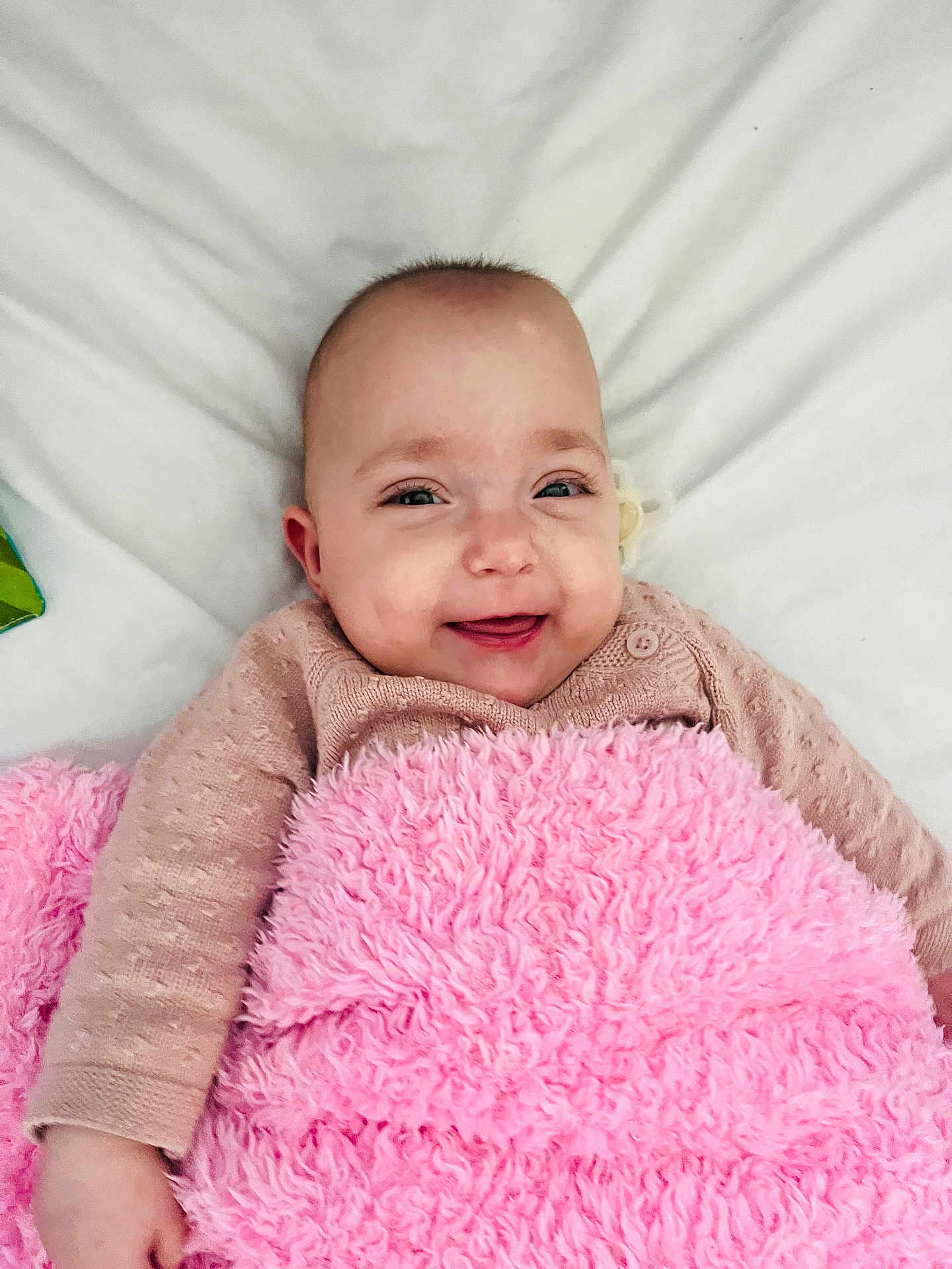 Aria is registered to the contest to win money with this photo: baby, smiling, blanket, pink, infant, cute, face, child, happy, lying_down, soft_texture, cozy, portrait, clothing, sleeves, skin, head, eyes, mouth, indoors