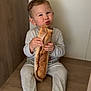 Izaac a rejoint le concours — aidez-le/la à gagner de superbes lots ! baguette, bench, bread, child, cozy, cute, expression, face, floor, food, hands, home, indoor, legs, light, pajamas, sitting, snack, toddler, wood