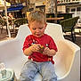 Izaac a rejoint le concours — aidez-le/la à gagner de superbes lots ! boy, cafe, chair, child, chocolate_egg, cute, daylight, food, gray_pants, outdoor, person, plastic_chair, playful, red_shirt, relaxing, snack, sunlight, table, toddler, umbrella