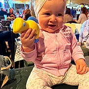 Ezra participe au concours pour gagner de l'argent avec cette photo : baby, blurry_background, casual_clothing, chair, child, cute, evening, hand, happy, headband, indoor, people, person, pink_hoodie, restaurant, seated, smiling, table, toddler, toy