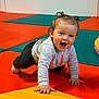 active, baby, black_pants, child, colorful, crawling, curly_hair, cute, fun, gray_jacket, happy, indoor, padded_floor, person, pigtails, play_area, playful, smiling, toddler, young_child