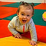 active, baby, child, colorful_mats, crawling, cute, fun, gray_jacket, green_mat, happy, indoor, infant, orange_mat, person, pigtails, pink_zipper, play_area, smiling, yellow_mat, young_child