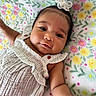 baby, infant, flower_headband, white_outfit, blanket, floral_pattern, cute, portrait, child, smiling, lying_down, skin, face, hand, soft_texture, colorful, adorable, young_child, happy, indoors