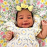 baby, smiling, infant, dress, headband, yellow_bow, floral_blanket, cute, happy, portrait, child, young, lying_down, patterned_clothing, adorable, skin, hand, face, cheerful, closeup