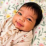 baby, infant, smile, face, eyes, blanket, floral_pattern, clothing, cute, portrait, indoors, soft_texture, child, young, happy, skin, head, closeup, lying_down, warm