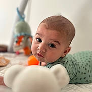 Elio participe au concours pour gagner de l'argent avec cette photo : baby, infant, face, eyes, teddy_bear, toy, bed, blanket, clothing, person, child, indoor, cute, curious, soft_light, closeup, portrait, focus, background_blur, lying_down