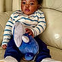 baby, child, striped_shirt, navy_pants, white_shoes, plush_toy, stuffed_animal, couch, leather, indoor, sitting, cute, curious, smiling, footwear, toy, person, infant, cozy, home