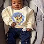Dany a rejoint le concours — aidez-le/la à gagner de superbes lots ! baby, child, infant, curly_hair, sweatshirt, cartoon_print, navy_pants, white_shoes, pacifier, baby_seat, indoor, cushion, floor_tiles, cute, comfortable, smiling, casual_clothing, portrait, closeup, seated