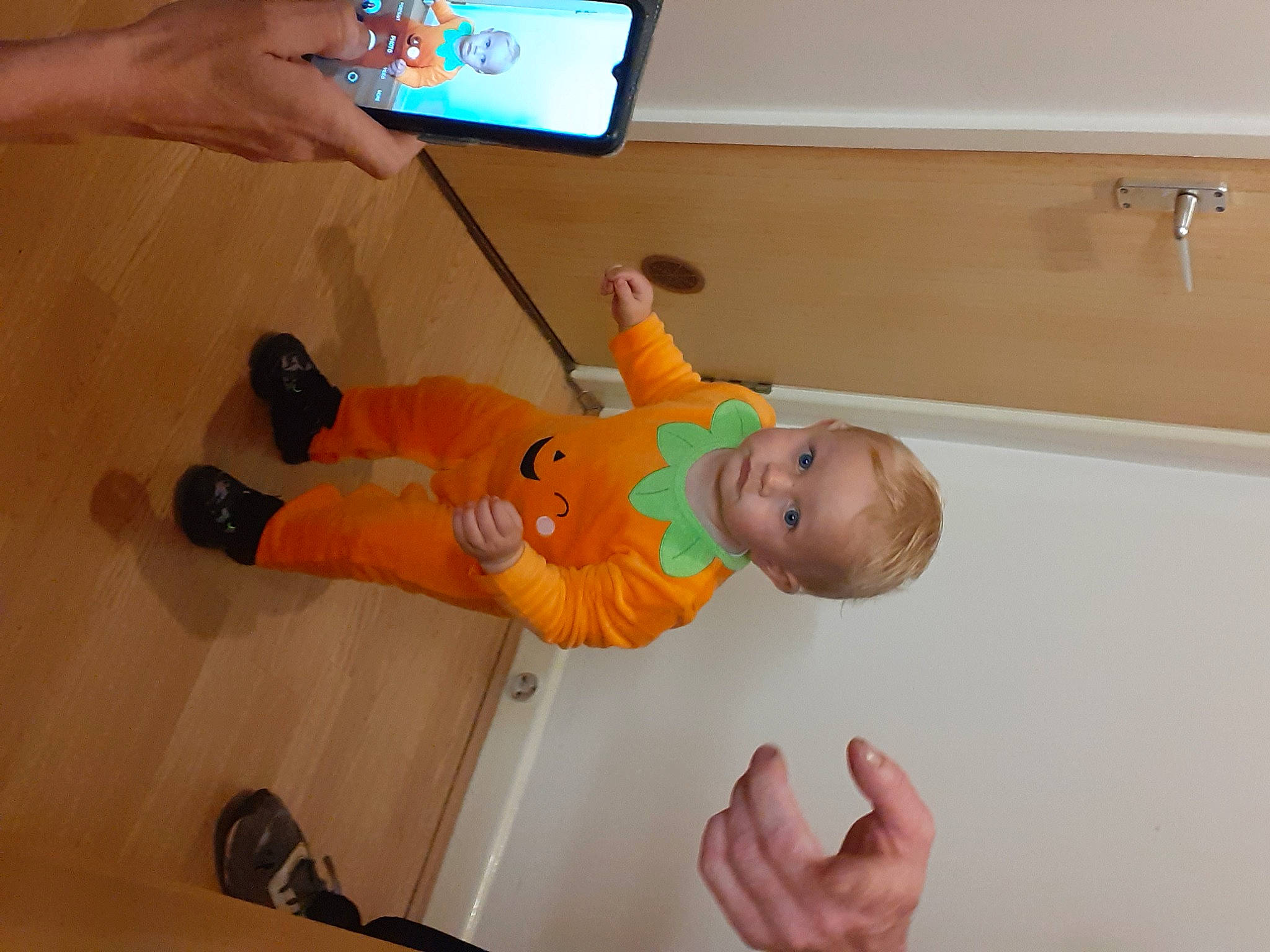 Harrison is registered to the contest to win money with this photo: baby, baby_products, baby_toddler_clothing, child, communication_device, finger, floor, flooring, fun, gadget, gesture, hand, hardwood, nail, person, play, room, thumb, toddler, wood