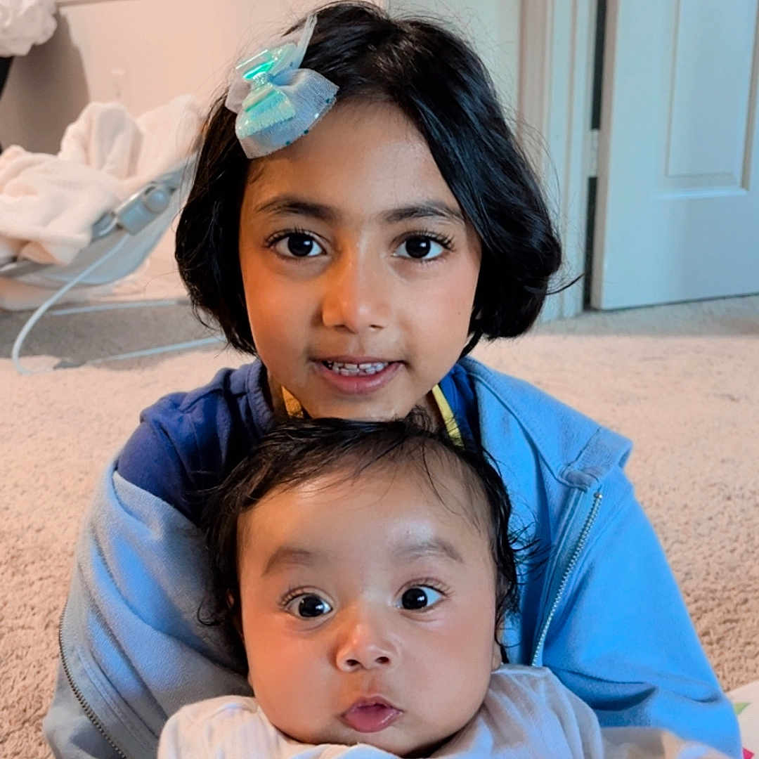 Vik joined the competition — help win amazing prizes! baby, blue_hoodie, carpet, child, closeup, cute, face, family, hair_accessory, happy, holding, home, indoor, infant, person, portrait, sibling, smile, white_pajamas, young_child