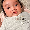 baby, carpet, child, clothing, curly_hair, cute, embroidery, expression, eyes, face, indoors, infant, long_eyelashes, lying_down, person, pink_blanket, portrait, skin, soft_texture, young