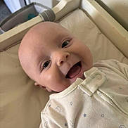 Elijah is registered to the contest to win money with this photo: baby, smiling, infant, onesie, white_clothing, face, head, happy, lying_down, indoor, crib, changing_pad, child, newborn, cute, skin, young, person, closeup, expression