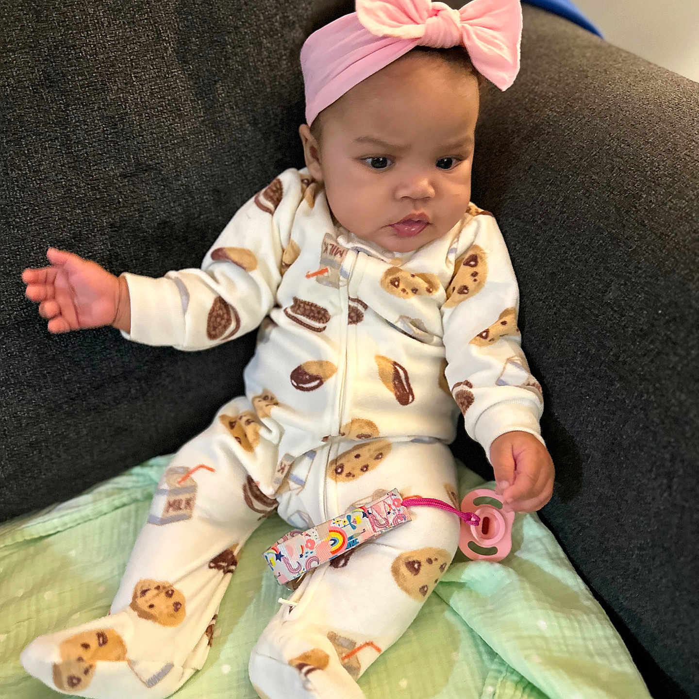 Jana is registered to the contest to win money with this photo: baby, blanket, child, clothing, cookie_pattern, couch, curious, cute, expression, headband, home, indoor, infant, pacifier, pajamas, patterned_clothing, person, pink, seated, soft_toys