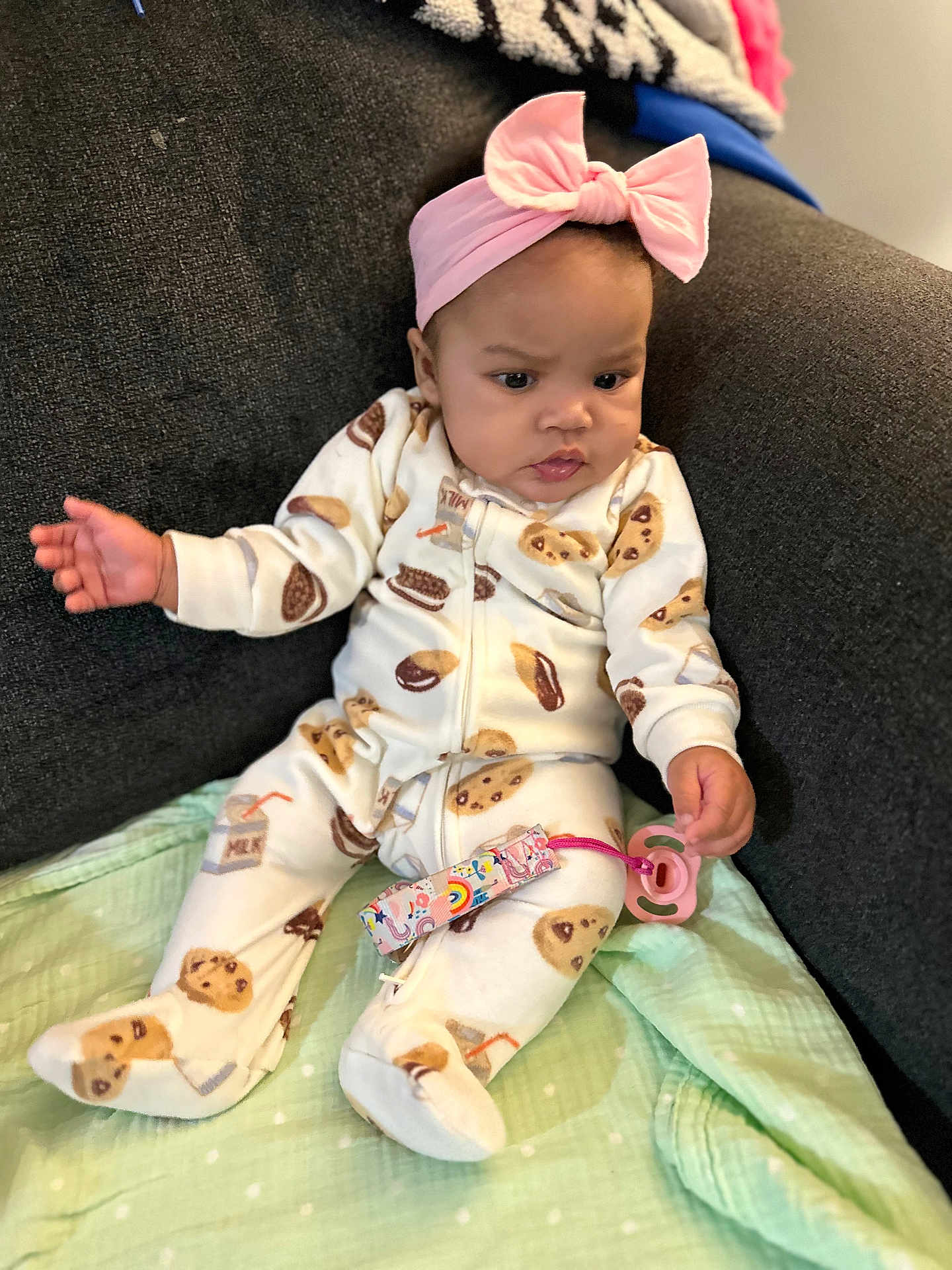 Jana is registered to the contest to win money with this photo: baby, child, indoor, pajamas, headband, pink, pacifier, blanket, couch, seated, patterned_clothing, cookie_pattern, expression, infant, soft_toys, clothing, person, cute, curious, home